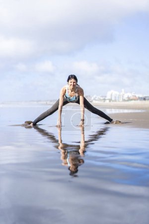 Téléchargez les photos : A woman doing stretching exercises at the beach while reflected on water - en image libre de droit
