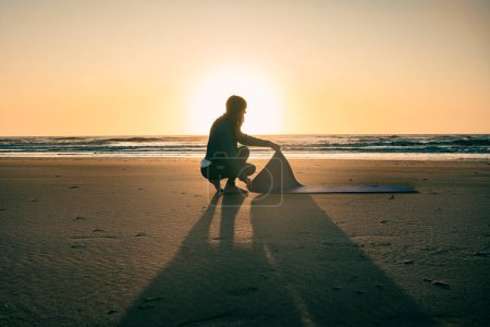 Téléchargez les photos : Silhouette of a  woman putting a yoga mat on the sand at sunrise - en image libre de droit