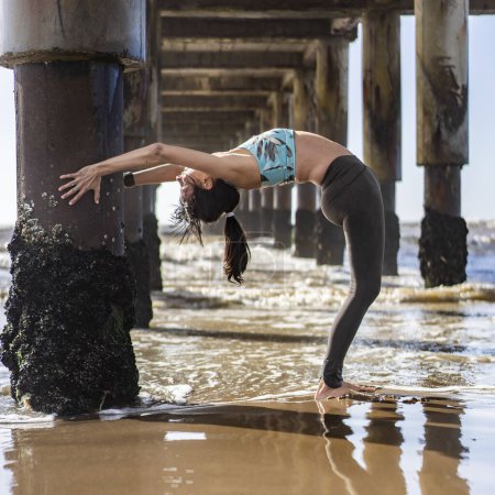 Photo for A woman doing stretching exercises under a pier at the beach - Royalty Free Image
