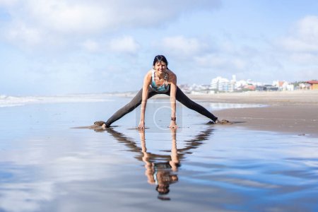 Photo for A woman doing stretching exercises at the beach while reflected on water - Royalty Free Image