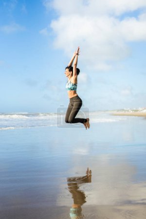 Téléchargez les photos : Woman jumping at the beach while reflected in the water - en image libre de droit