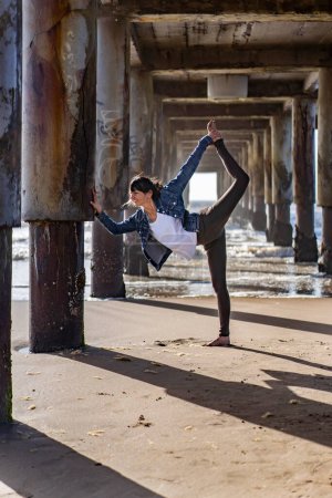 Téléchargez les photos : A woman practicing yoga outdoors, doing Standing Bow (Dandayamana Dhanurasana) pose. - en image libre de droit