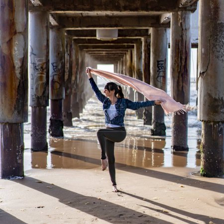 Photo for Woman dancing under a pier holding a scarf on the wind. - Royalty Free Image