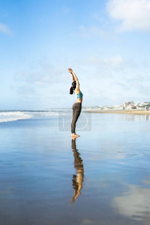 Téléchargez les photos : A woman practicing yoga on the water at the beach, doing Crescent Moon (Ardha Chandrasana) pose. - en image libre de droit