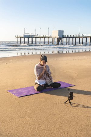 Foto de Slim woman yoga instructor giving online yoga training in a mobile phone camera. Yoga and meditation for social net. - Imagen libre de derechos