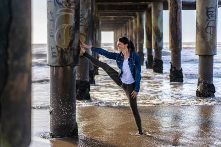 Téléchargez les photos : Smiling woman doing stretching exercises on the water at the beach - en image libre de droit