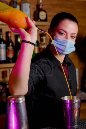 Téléchargez les photos : Young woman bartender makes a cocktail with face mask - en image libre de droit