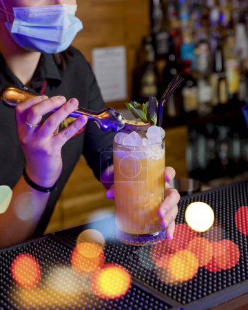 Photo for Young woman bartender makes a cocktail with face mask - Royalty Free Image