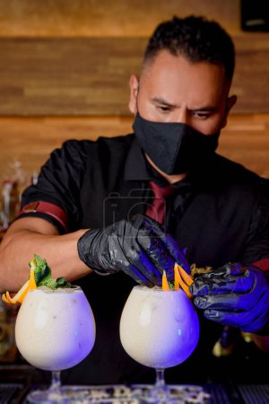 Téléchargez les photos : Black man bartender with mask preparing a cocktail. drinks concept - en image libre de droit