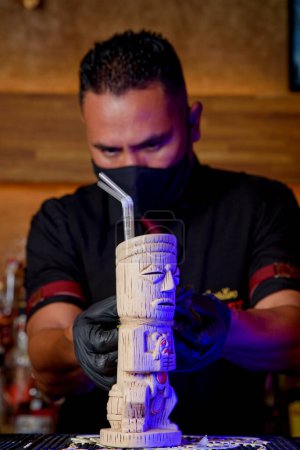 Téléchargez les photos : Bartender with mask preparing cocktail at a bar counter - en image libre de droit