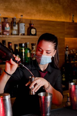 Foto de Young woman bartender makes a cocktail with face mask - Imagen libre de derechos