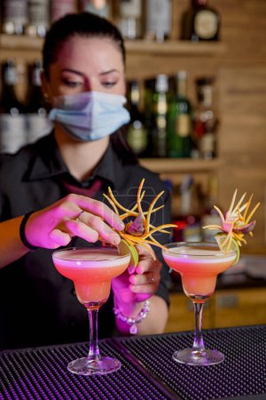 Téléchargez les photos : Young woman bartender makes a cocktail with face mask - en image libre de droit