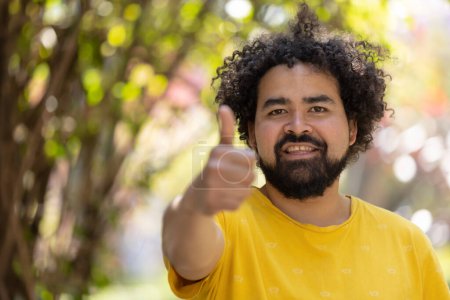 Téléchargez les photos : Portrait of a Mexican man smiling with afro and beard thumbs up - en image libre de droit