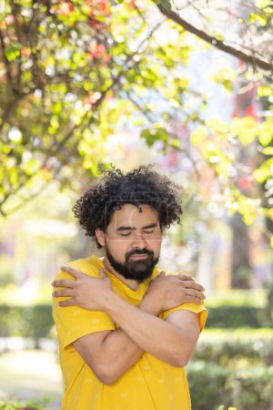 Foto de Young Mexican man with beard and afro hugging himself, self love - Imagen libre de derechos