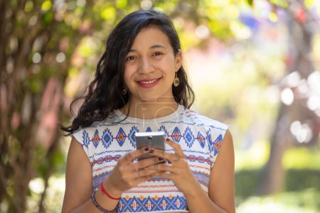 Foto de Real Mexican woman holding smart phone and looking at camera - Imagen libre de derechos