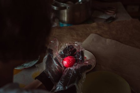 Téléchargez les photos : Girl in plastic gloves paints red Easter egg - en image libre de droit