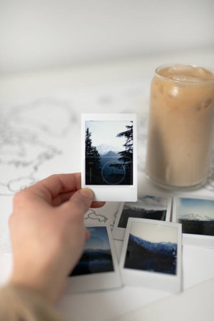 Téléchargez les photos : Hand Holding Polaroid Photo of Mountain on World Map with Iced Coffee - en image libre de droit