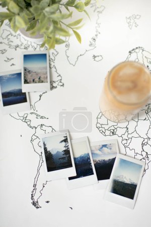 Foto de Polaroid Photos on Travel World Map with Iced Coffee and Plant - Imagen libre de derechos