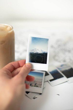 Foto de Hand Holding Mountain Polaroid Photo on World Map with Iced Coffee - Imagen libre de derechos