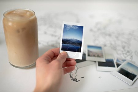 Téléchargez les photos : Photo de Polaroïd de montagne tenue à la main sur la carte du monde avec du café glacé - en image libre de droit
