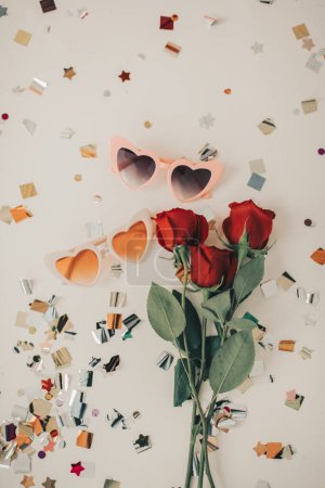 Foto de Gafas de sol en forma de corazón con rosas rojas y formas coloridas de confeti - Imagen libre de derechos