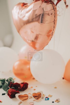 Téléchargez les photos : Lunettes de soleil coeur à côté de confettis, roses et ballons pour les vacances - en image libre de droit