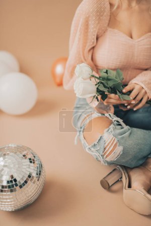 Téléchargez les photos : Gros plan d'une femme assise tenant des roses blanches près d'une balle disco - en image libre de droit