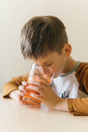 Foto de Niño blanco bebiendo jugo de naranja en la mañana en la mesa - Imagen libre de derechos