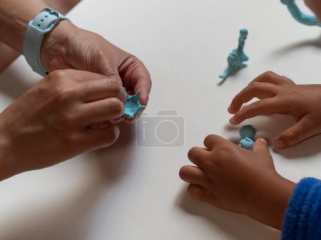 Foto de Niño y madre jugando con coloridas figuras de arcilla de dinosaurio. - Imagen libre de derechos
