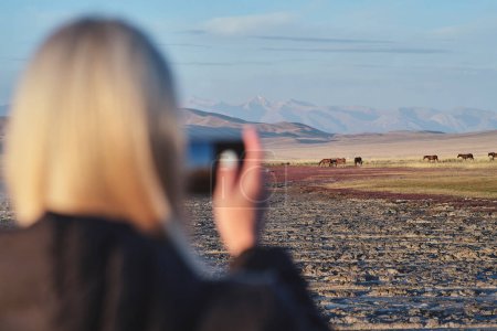 Photo for A woman takes a photo of horses, Tuz-Kol lake, Kazakhstan, - Royalty Free Image