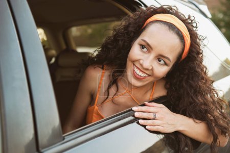 Téléchargez les photos : La fille regarde par la fenêtre de la voiture et sourit - en image libre de droit