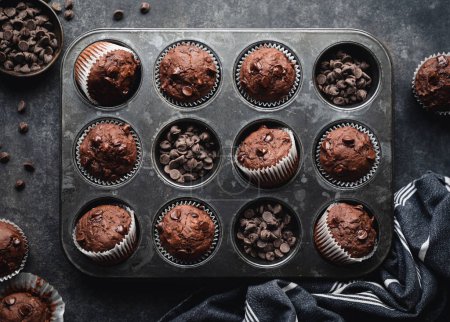 Téléchargez les photos : Overhead of tin of chocolate zucchini muffins on black background. - en image libre de droit