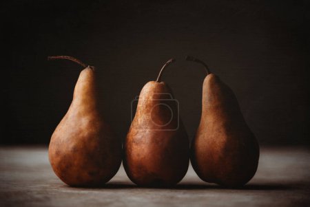 Foto de Close up of three brown bosc pears against dark background. - Imagen libre de derechos