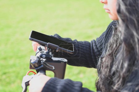 Téléchargez les photos : Jeune femme latina, chevauchant un scooter électrique et utilisant un smartphone - en image libre de droit