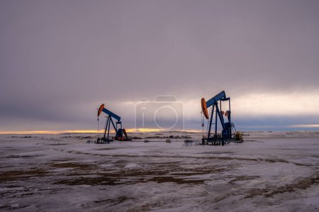 Téléchargez les photos : Pump jacks drawing crude oil from deep under ground on a moody Alberta morning in winter. - en image libre de droit
