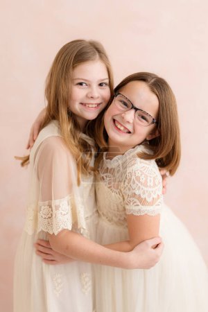 Photo for Sister's hugging indoors against pink backdrop - Royalty Free Image