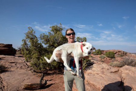 Foto de Mujer joven con gafas de sol sosteniendo al perro en Dead Horse Point, Utah - Imagen libre de derechos