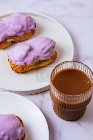 Foto de Eclair in purple berry glaze and coffee with milk in a glass - Imagen libre de derechos