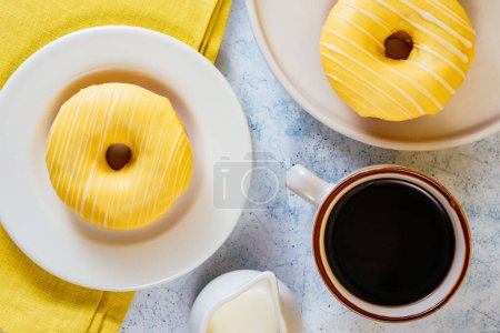 Téléchargez les photos : Lemon doughnuts in yellow glaze, coffee in a glass. - en image libre de droit