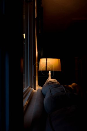 Téléchargez les photos : Lampe de Table Unique Illuminée dans les Ombres Sombres du Jour de Pluie dans le Salon - en image libre de droit