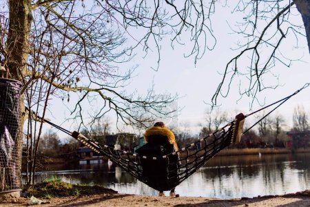 Téléchargez les photos : Personne assise dans un hamac accroché à deux arbres contre la rivière - en image libre de droit