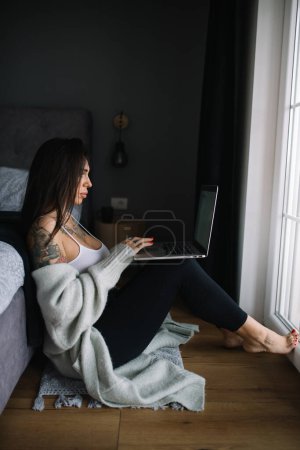Téléchargez les photos : Femme tatouée travaillant sur un ordinateur portable assis sur le sol - en image libre de droit