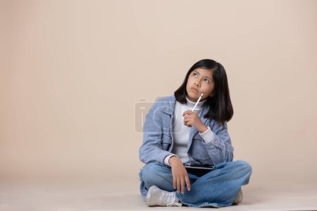 Photo for Mexican girl sitting on the floor thinking expression with table - Royalty Free Image