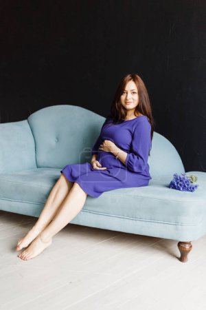 Photo for Pregnant happy woman in a blue shirt is smiling while expecting a baby - Royalty Free Image
