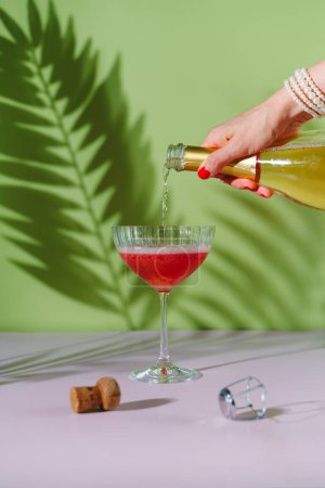 Téléchargez les photos : Une main de femme avec une manucure rouge verse du champagne dans un verre. - en image libre de droit