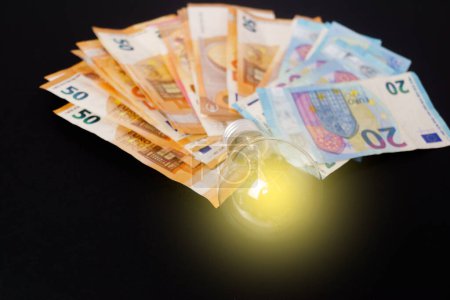 Téléchargez les photos : Ampoule allumée avec billets en euros en arrière-plan - en image libre de droit