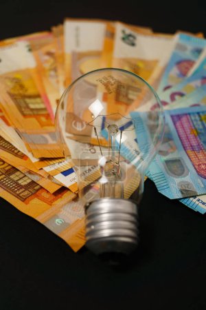 Photo for Lighted light bulb with euro banknotes in the background on a black background, concept of rising electricity prices - Royalty Free Image