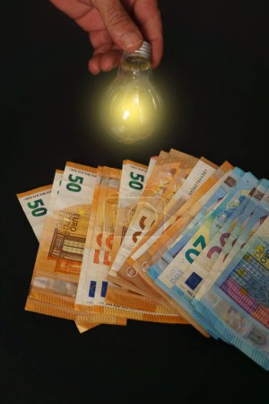 Photo for Lighted light bulb with euro banknotes in the background on a black background, concept of rising electricity prices - Royalty Free Image