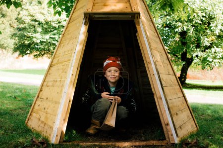 Photo for Boy sitting smiling in a wooden tipi outside playing - Royalty Free Image