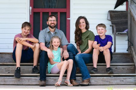 Heureuse famille de cinq personnes assise sur les marches de la ferme.